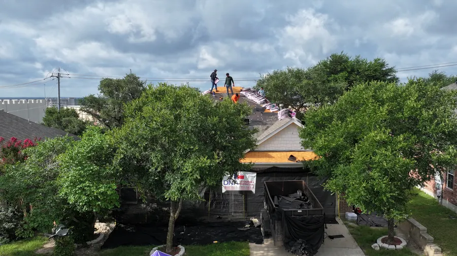 Drone photo of the Catch-All debris netting system set up around a San Antonio home during a DNA roof replacement, with the dump trailer in the driveway